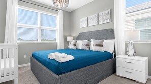 A bedroom with a bed, nightstands, a crib, and artwork on the wall.
