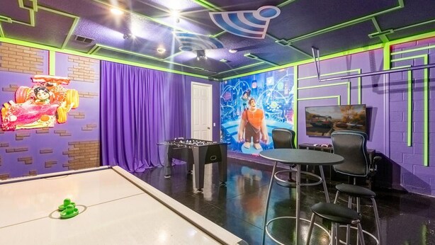 A room with a foosball table, a billiards table, and a television.