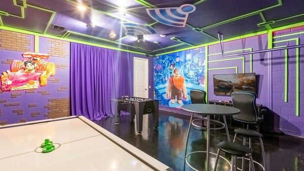 A room with a foosball table, a billiards table, and a television.