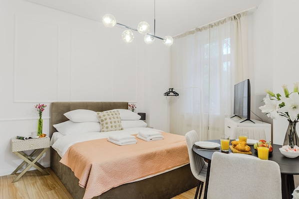 A neatly arranged hotel room with a bed, bedside table, and a dining area with breakfast items. - Apartament Ogrodowa 26a (Warsaw)