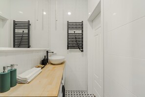 A modern bathroom with a wooden vanity, white tiles, a large mirror, two towel racks, and a black and white patterned floor. - Apartament Ogrodowa 26a (Warsaw)