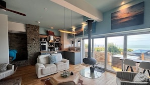 Una sala de estar moderna con chimenea, una zona de cocina y ventanas amplias que dan al mar.