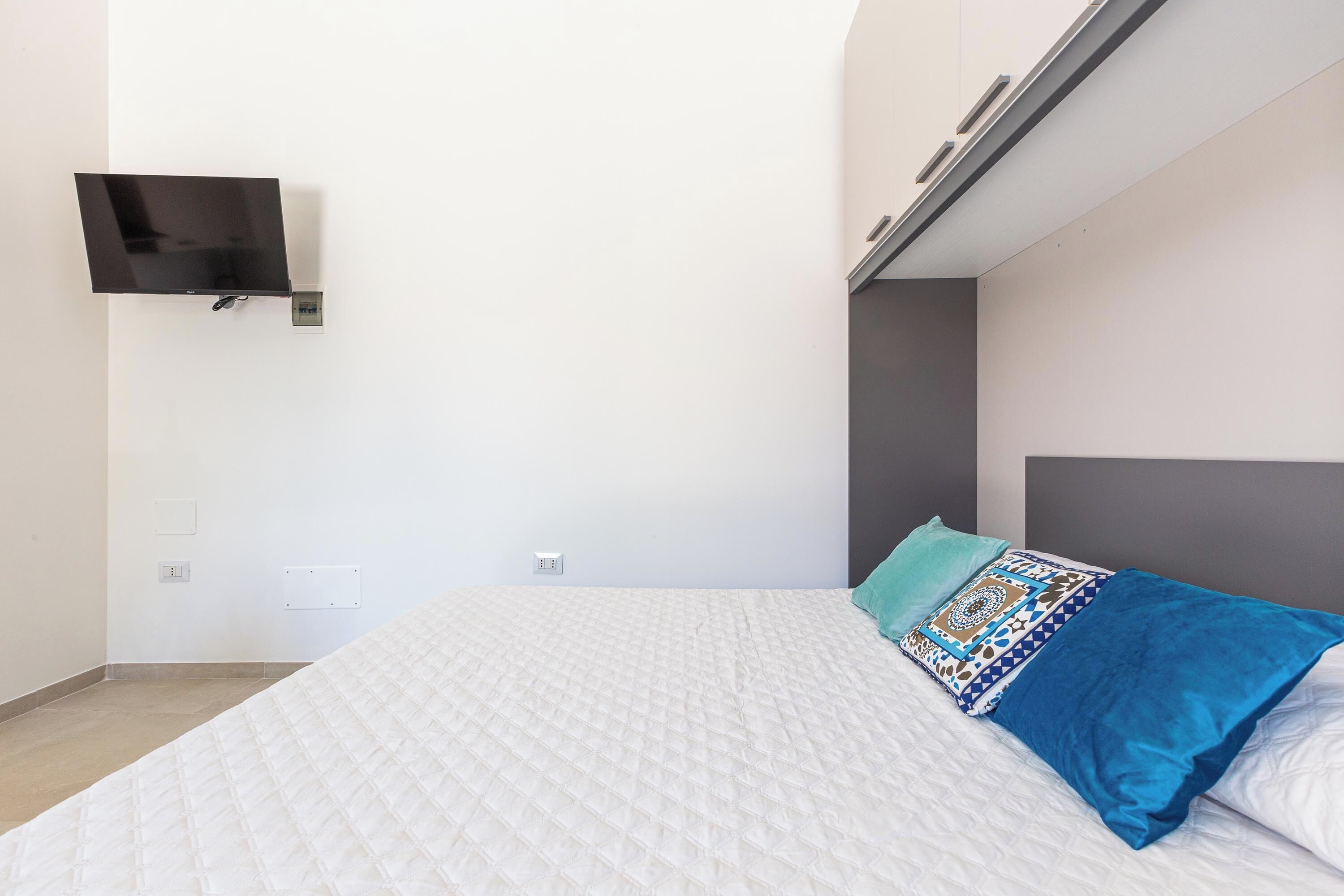 A bedroom with a bed, a TV mounted on the wall, and a headboard.