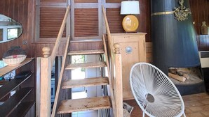 Eine Holztreppe führt zu einem erhöhten Bereich mit einem großen Kamin, einem weißen Sessel und einem Schädel als Dekoration an der Wand.