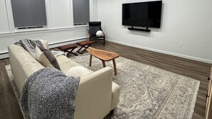 A modern living room with a large sofa, a coffee table, and a flat-screen TV mounted on the wall.