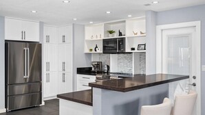 Eine moderne Küche mit weißen Schränken, einem Edelstahlkühlschrank, einer schwarzen Mikrowelle und einer Kaffeemaschine auf der Kücheninsel.