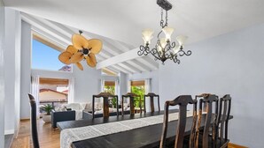 Ein Essbereich mit einem langen Tisch, Stühlen, einer Chandelier und einem Deckenventilator.