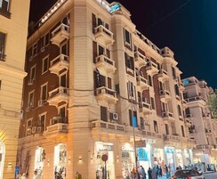 A multi-story hotel with balconies, ground-level shops, and a well-lit facade.