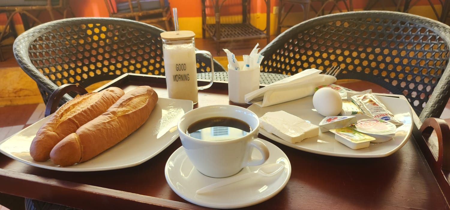 A breakfast tray with croissants, a cup of coffee, a milk jug, and various condiments on a table.