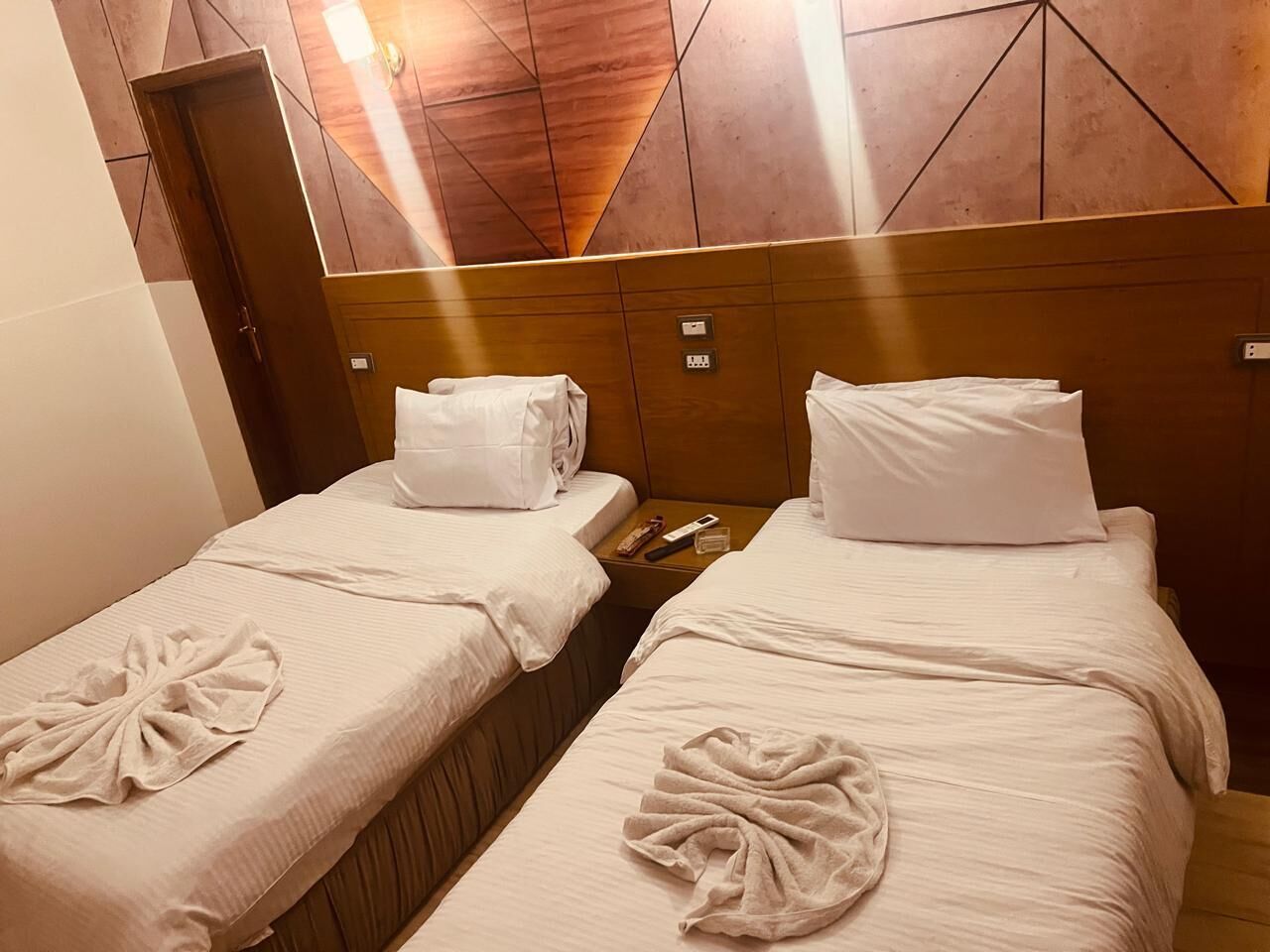 Ett hotellrum med två separata sängar, där varje säng har en prydligt vikt handduk och en kudde.