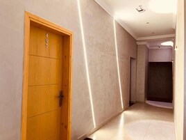 Un couloir avec une porte en bois portant le numéro 407, qui donne sur une pièce où se trouve une armoire de couleur sombre.