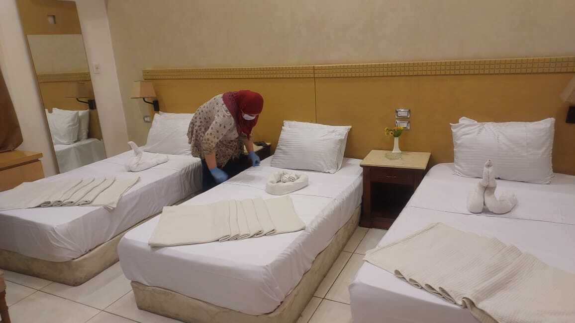A hotel room with two beds, each with white linens and pillows, a nightstand with a lamp, and a mirror on the wall.
