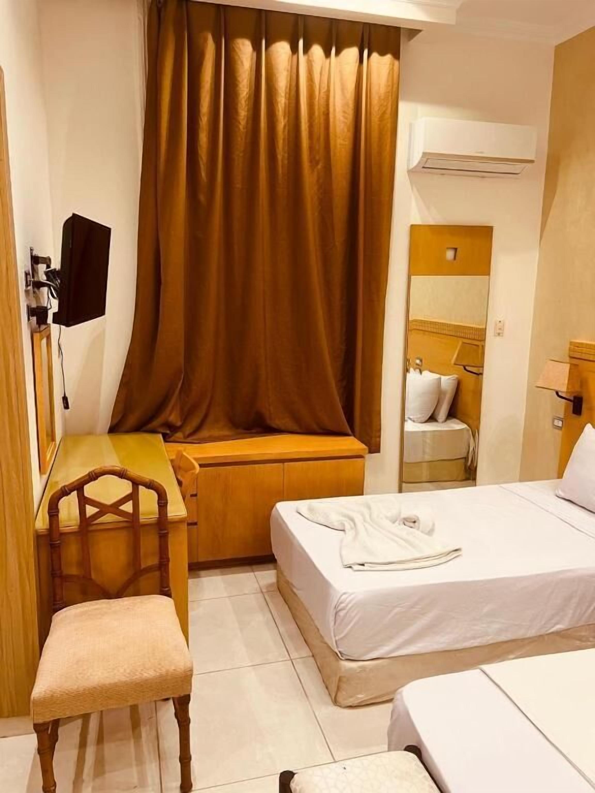 Ett hotellrum med en säng, ett skrivbord, en stol, en spegel och en luftkonditioneringsanläggning.