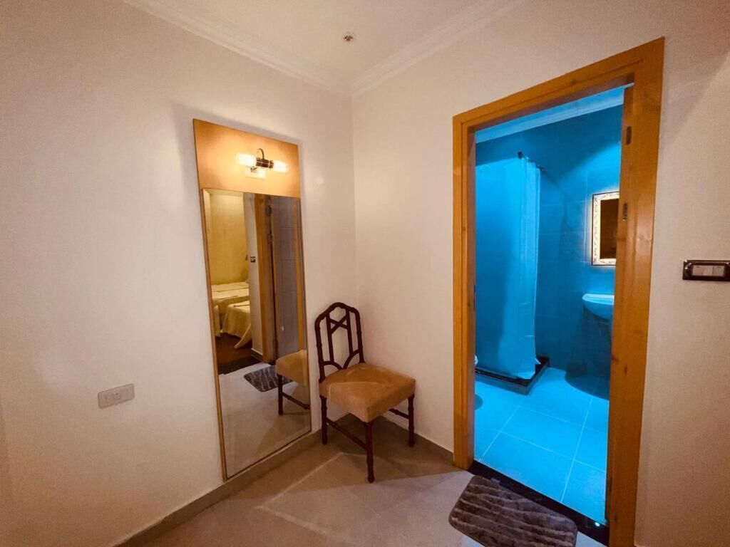 A hallway with a mirror, a chair, and a bathroom visible through an open door.