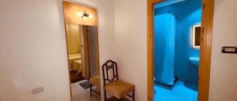 A hallway with a mirror, a chair, and a bathroom visible through an open door.