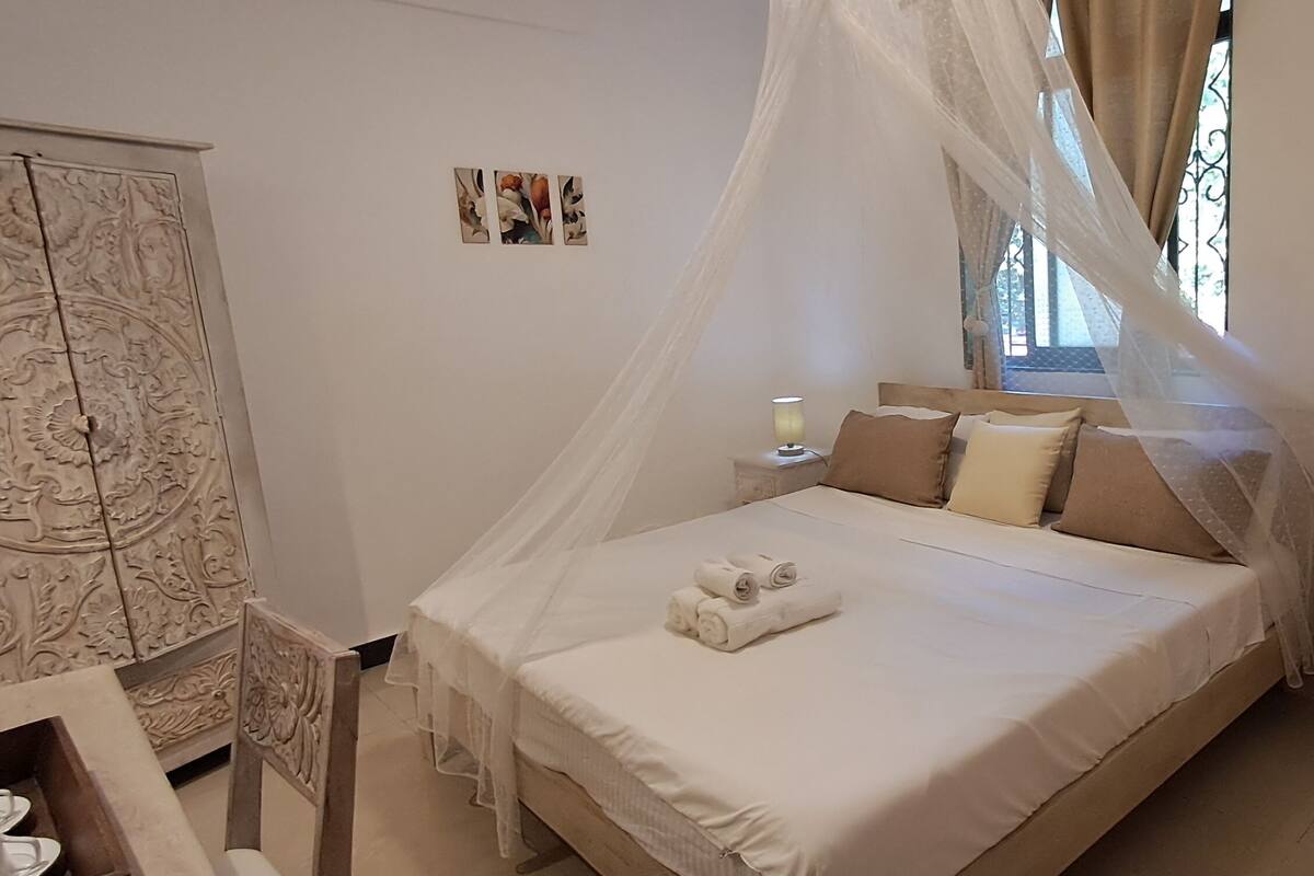A bedroom with a bed, bedside lamps, a nightstand, a wardrobe, and artwork on the walls.