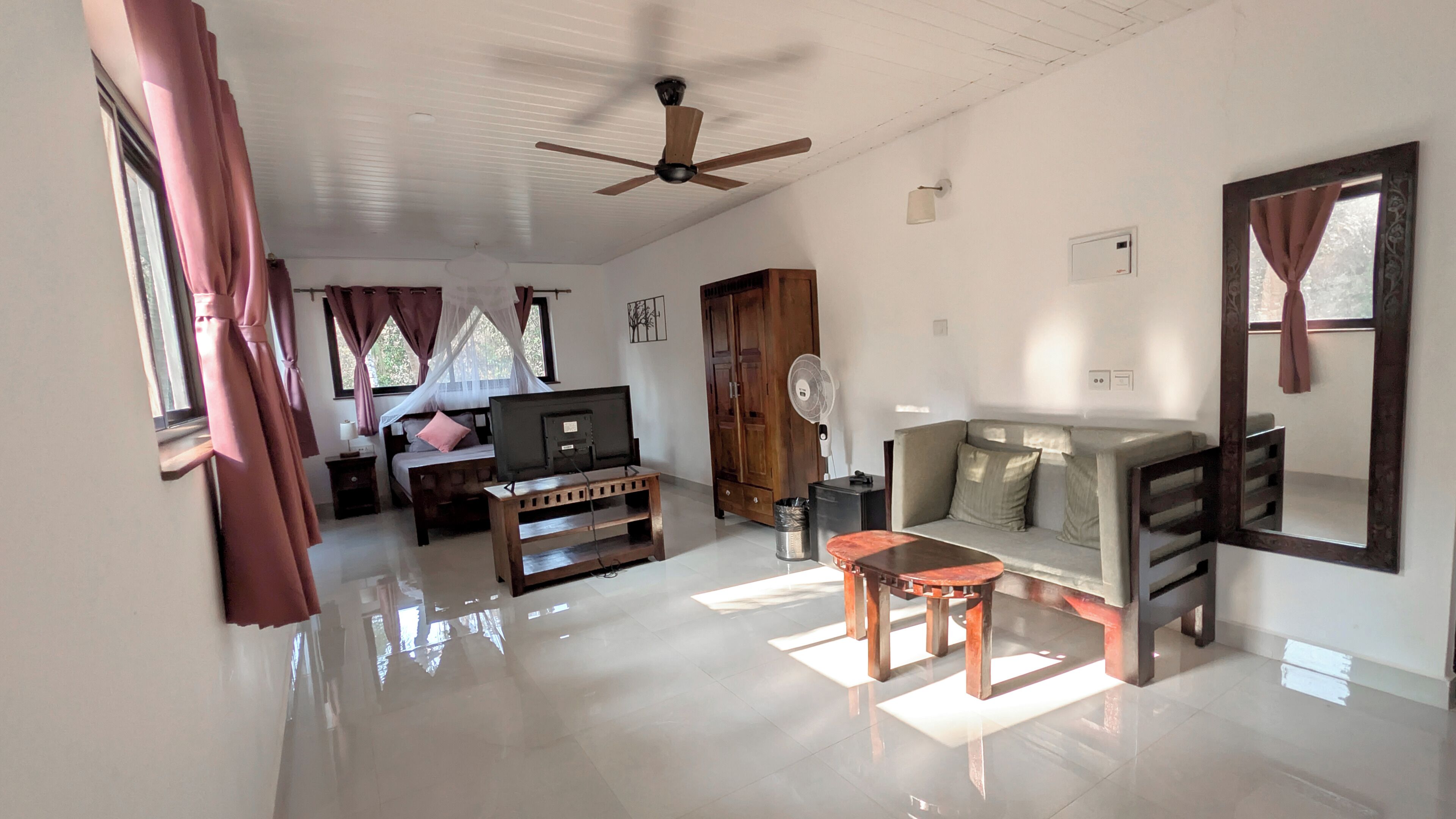 A spacious living area with a ceiling fan, a sofa, a TV, and a dining table.