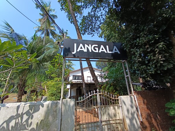 A sign reading "JANGALA" with a gated entrance, surrounded by lush greenery and a white building in the background. - Jangala Resort (Baga)