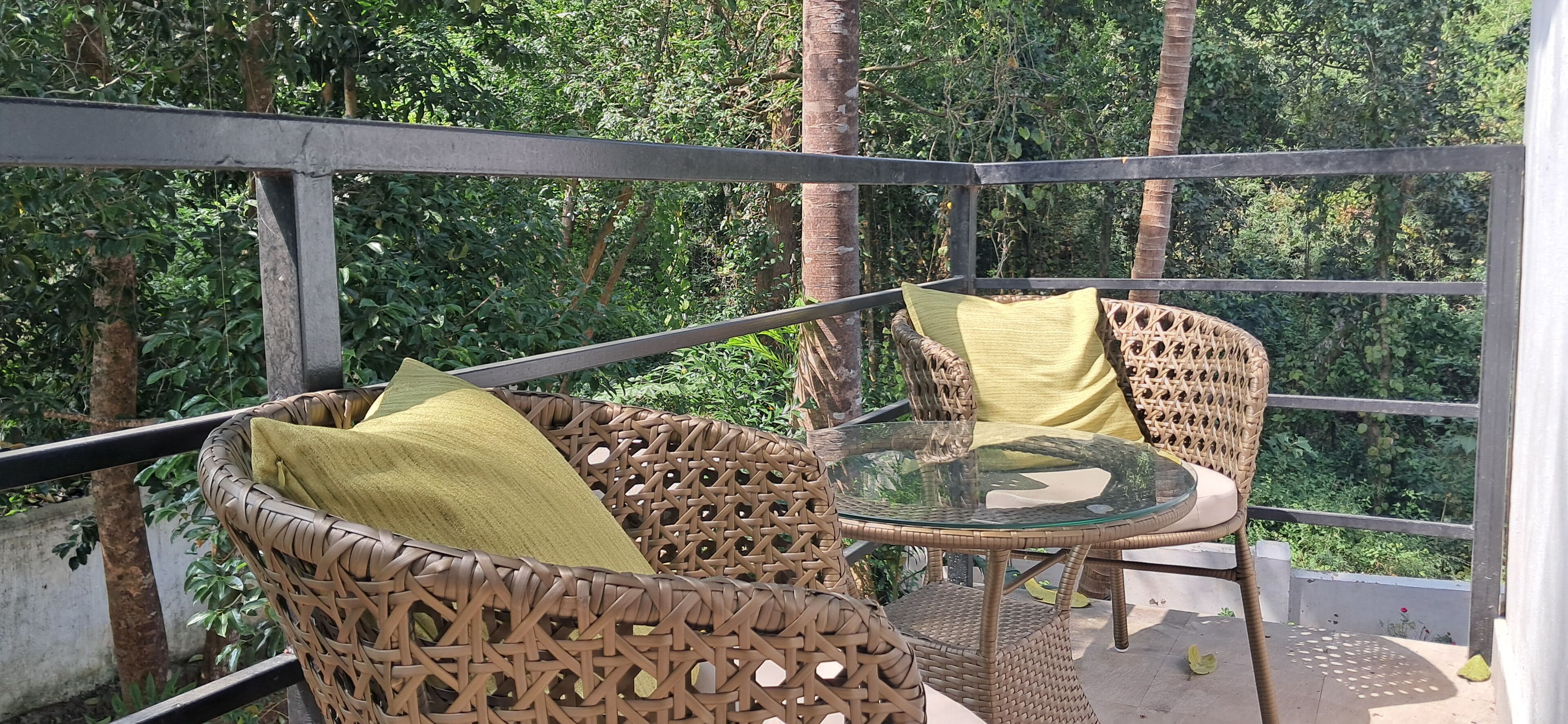 Ein Balkon mit Korbmöbeln und einem Glastisch, umgeben von viel Grün.