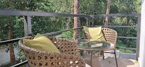 A balcony with wicker furniture and a glass table, surrounded by greenery. - Jangala Resort (Baga)