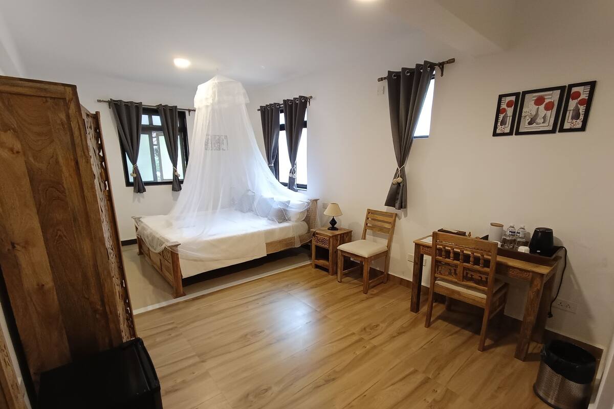 A bedroom with a bed, a chair, a desk, and a trash bin.