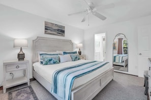 A bedroom with a bed, nightstands, a ceiling fan, a painting, and a mirror. - J-358 - Corner Unit, Updated And Near Lobby (Naples)
