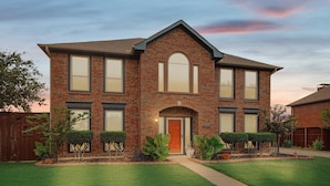 A two-story brick house with a central entrance, large windows, and a well-maintained lawn. - Vista Valley Vacay, 5-BD w Pool & Cinema (Lewisville)