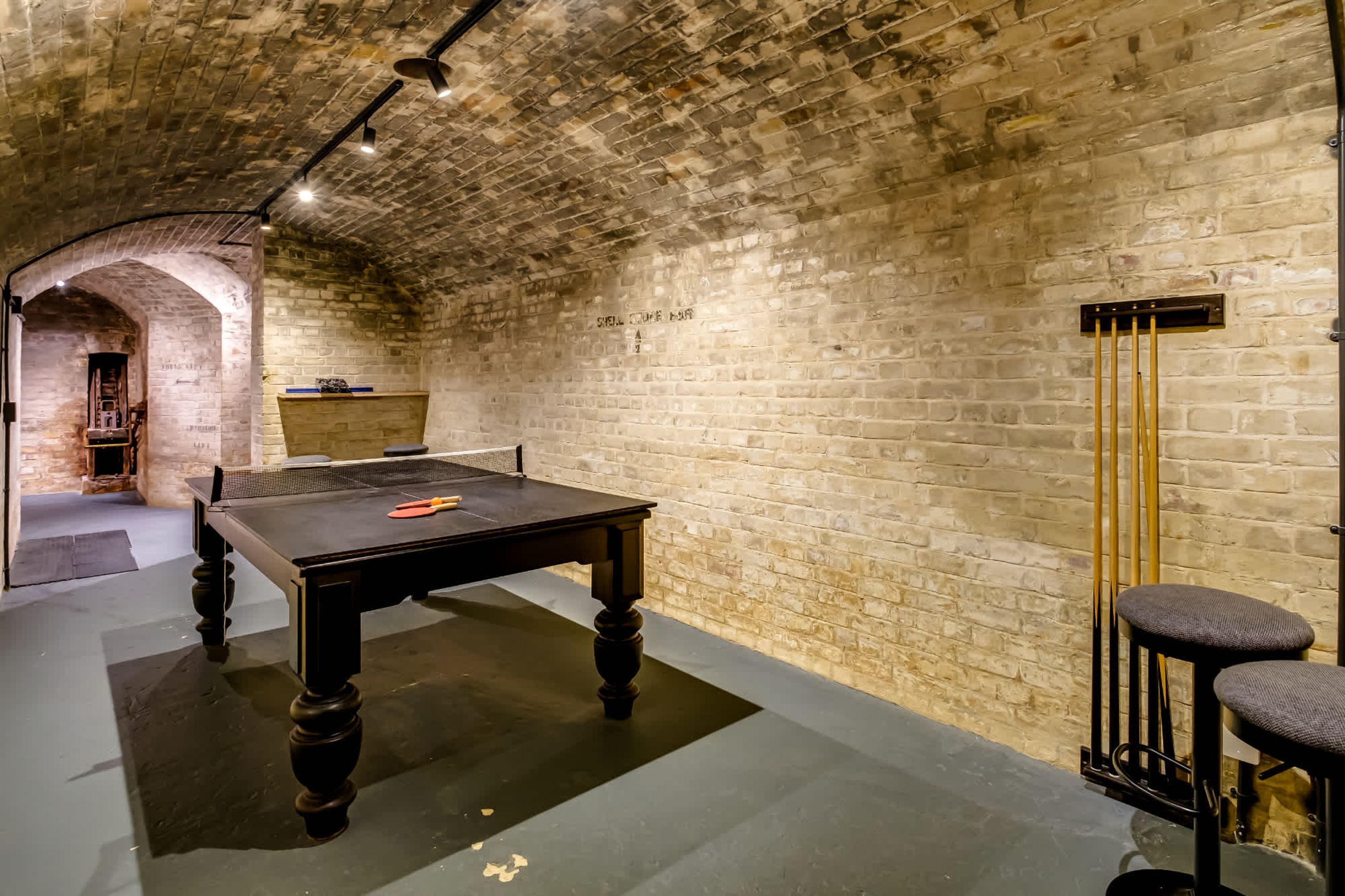 Une table de billard dans une pièce aux murs en briques et à l’entrée en forme d’arc.