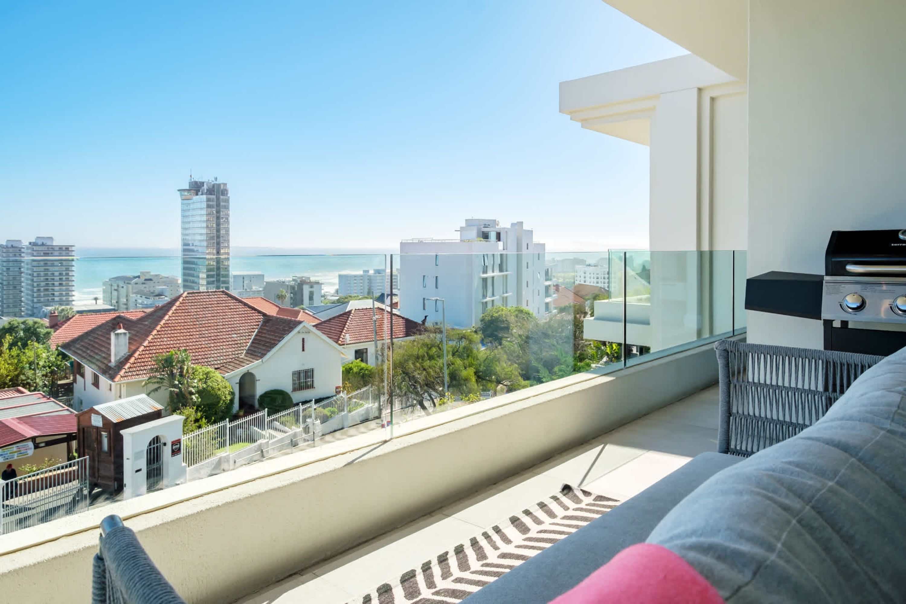 Ein Balkon mit Blick auf Stadt und Meer, eine Couch und ein Grill.