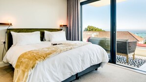 A modern hotel room with a large bed, a balcony with a view of the sea, and a dining area with a table and chairs. - Charming Coastal Escape Marula One (Cape Town)