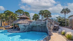Une piscine dotée d’une structure surmontée d’un toit de chaume, d’un mur en pierres apparentes et d’un patio dallé avec des espaces de détente en plein air.