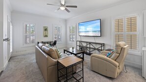 Un salon avec un canapé beige, un fauteuil inclinable, une table basse et un téléviseur fixé au mur.