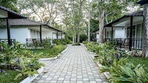 A pathway leading to two white buildings with balconies, surrounded by lush greenery and trees. - Silver Oak Tropical Resort By Bay Hotels (Uran)