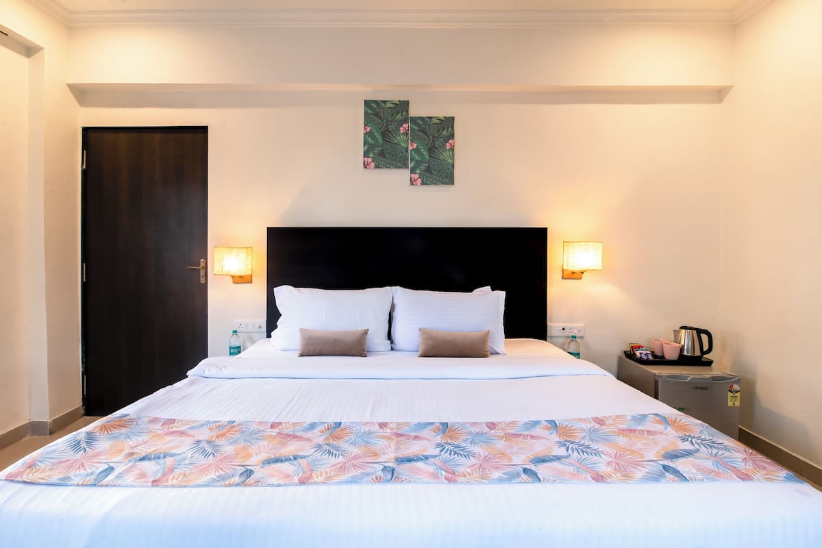 Una habitación de hotel con una cama grande, dos lámparas fijadas a la pared, una mesita de noche con cafetera y una puerta.