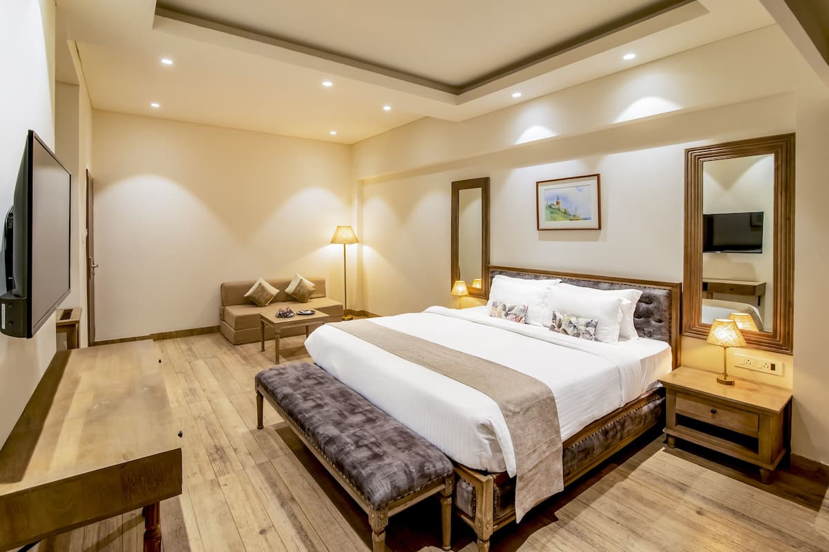 Un dormitorio con una cama grande, mesitas de noche, un banco, un televisor y una lámpara.
