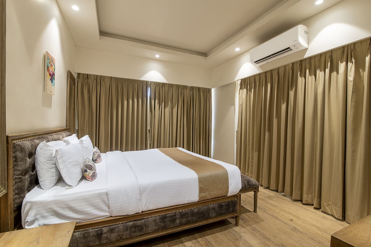 Una cama bien tendida con sábanas blancas y detalles en marrón, un cabecero de madera y una mesita de noche de madera con una lámpara.
