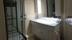 A bathroom with a glass shower enclosure, a white sink, and a large mirror above the vanity.