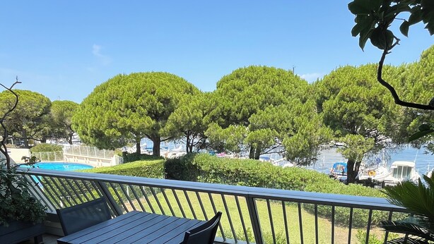 Un balcone con tavolo e sedie, affacciato su un'area d'acqua con barche e alberi.