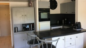 Una cucina compatta con un piano di lavoro nero, mobili bianchi, un forno a microonde, una macchina da caffè e una sveglia appesa al muro.