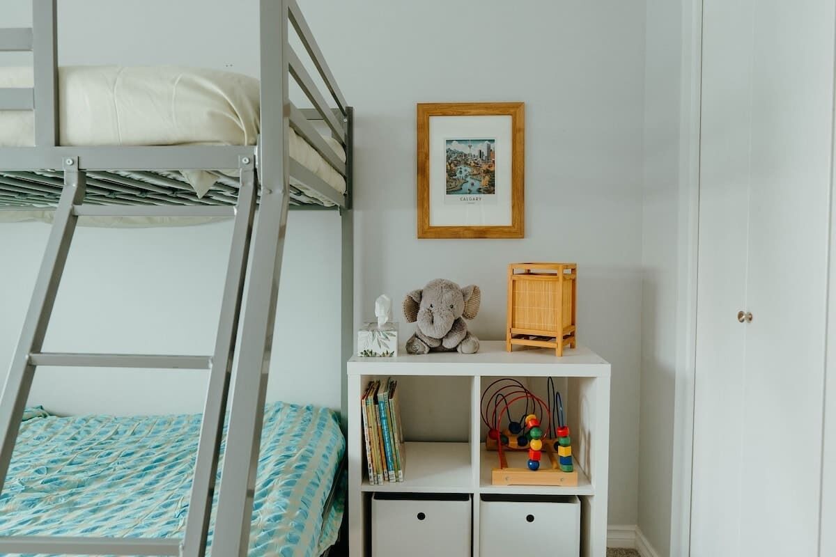 Een stapelbed, een ingelijst beeld, een knuffel en een houten speelgoedje op een witte plank.