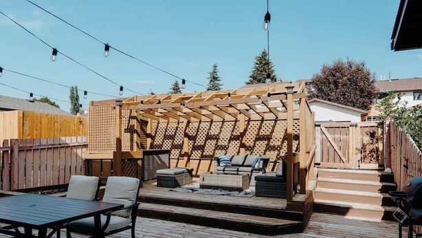 Eine Terrasss mit Holz-Pergola, Sitzgelegenheit und Grill.