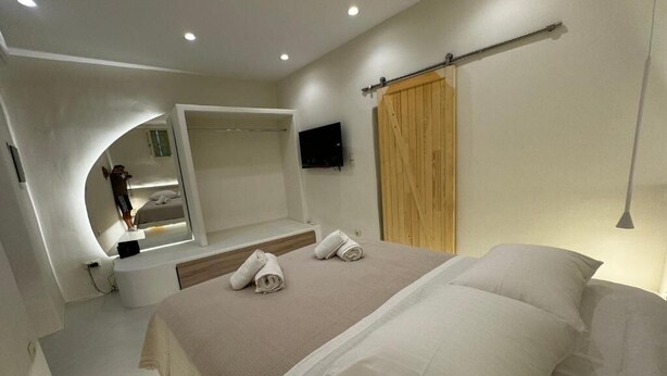 Une chambre à coucher moderne avec un grand lit, une armoire en bois, un téléviseur fixé au mur et un miroir incurvé.