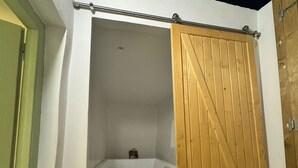 Une salle de bain avec une baignoire, une porte en bois et une porte verte.