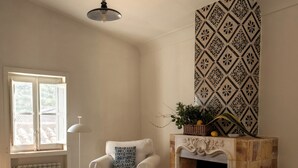 Un salon avec une cheminée, un fauteuil blanc, des meubles en osier et un papier peint à motifs.