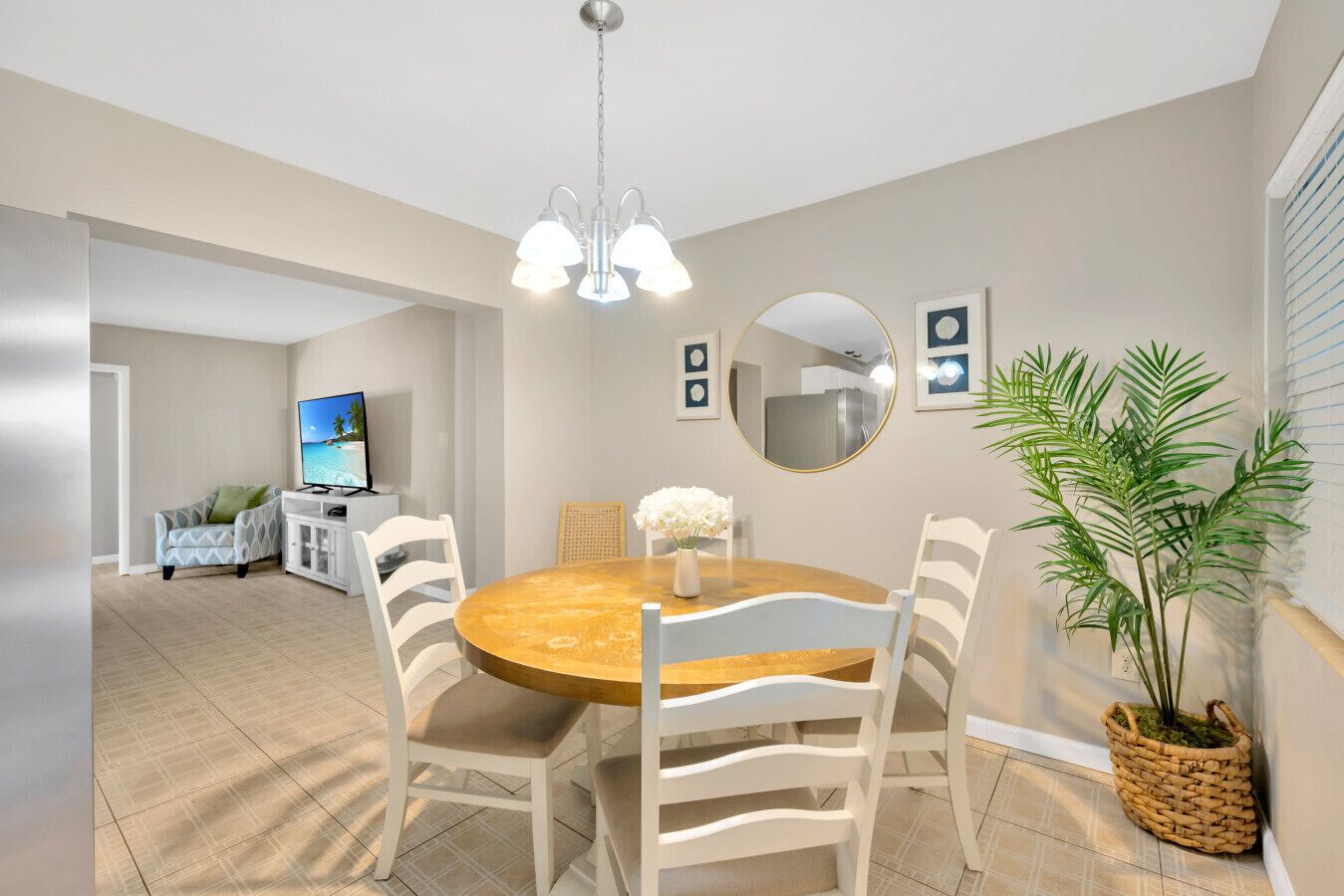 A modern dining area with a round table, white chairs, a chandelier, and a potted plant.