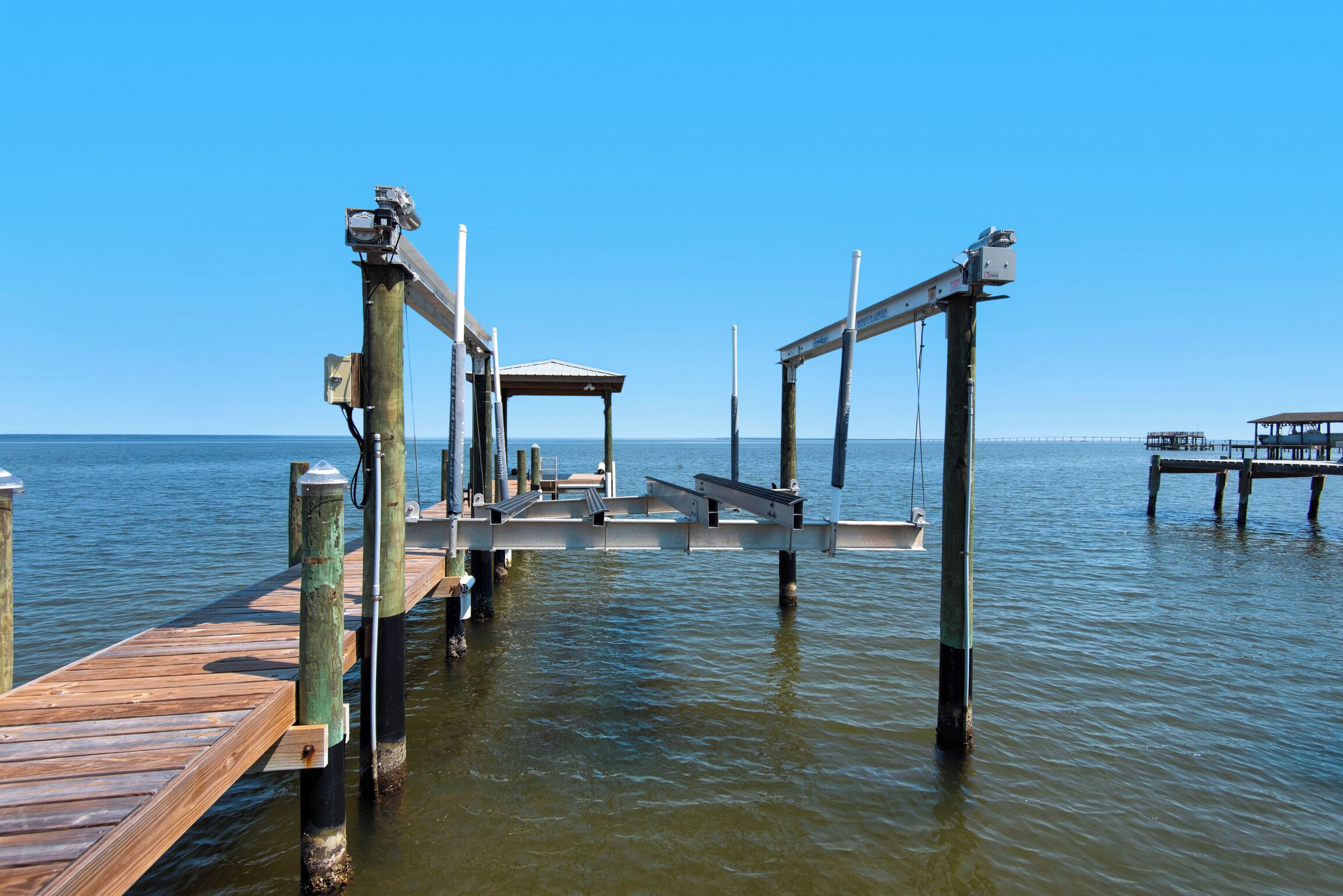 Un muelle de madera se extiende sobre aguas tranquilas, con un área de descanso cubierta y un pequeño bote amarrado cerca.