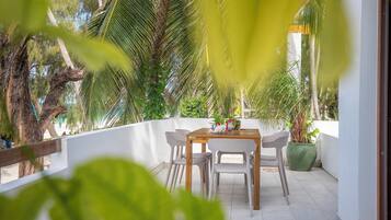 Une terrasse avec une table et des chaises, entourée de plantes en pot et de palmiers.