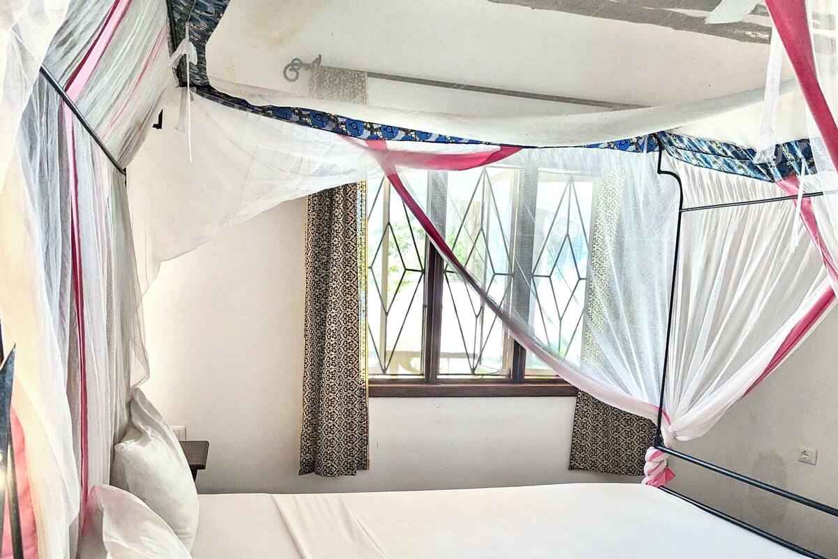 A single bed with a canopy, white bedding, and patterned curtains.