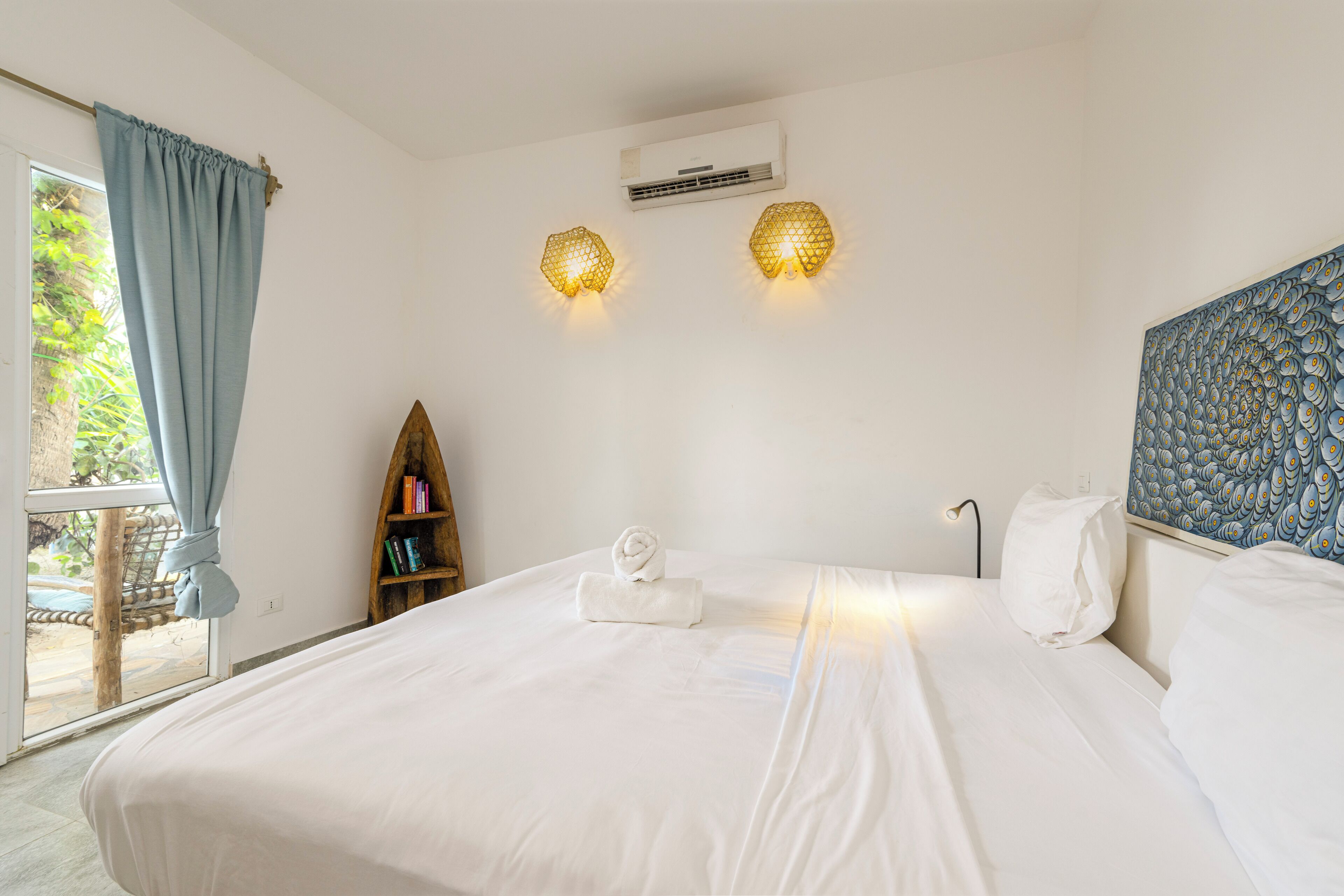 Habitación de hotel con una cama grande, una estantería, un equipo de aire acondicionado y una ventana con cortinas.
