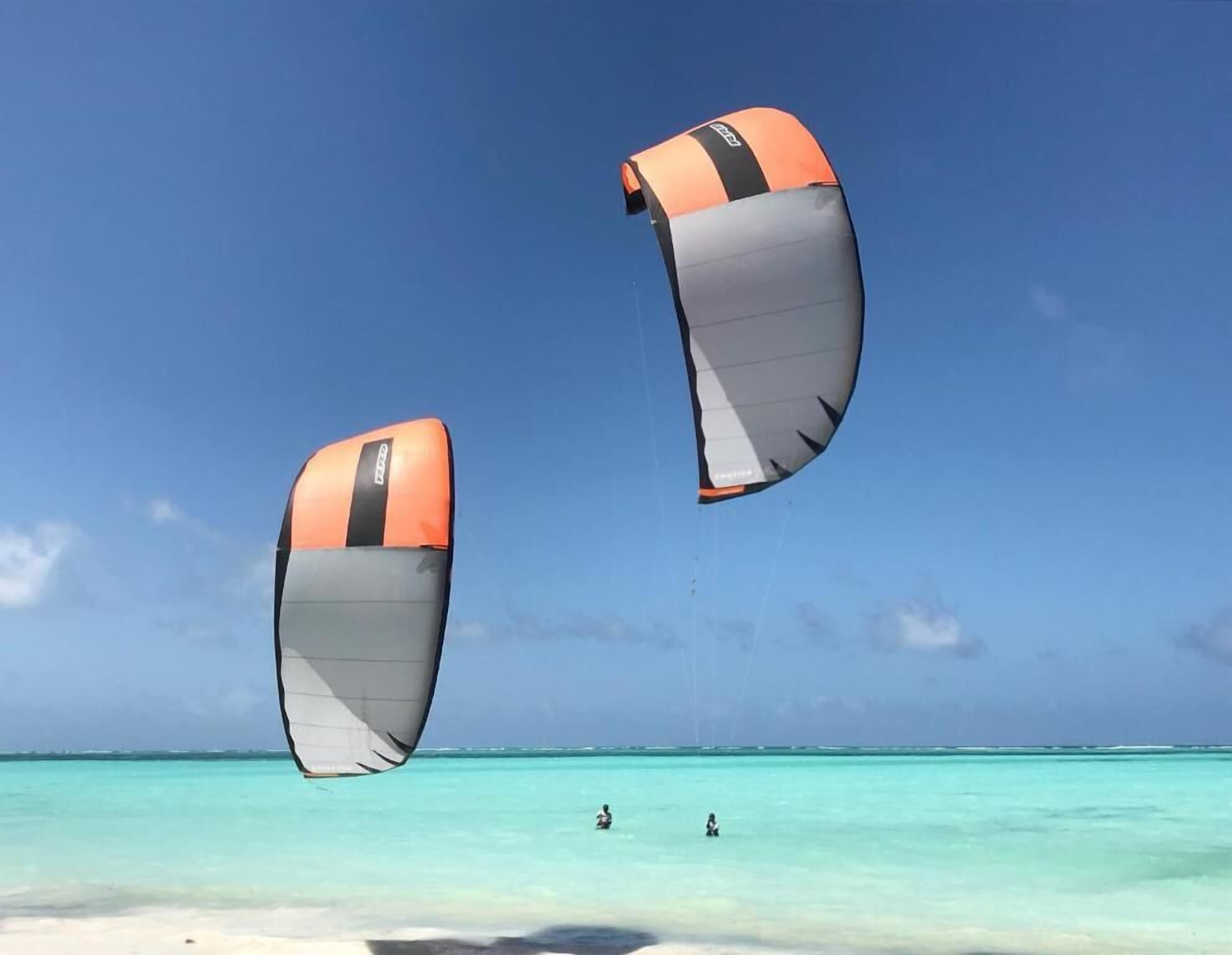 Uma praia com águas turquesa cristalinas e dois pipas voando no céu.
